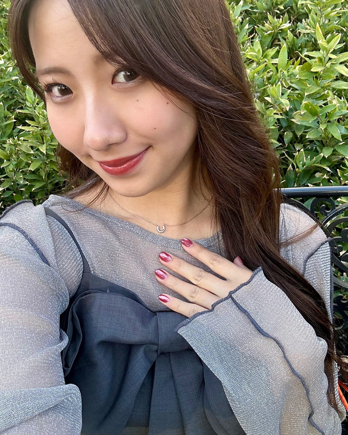 リボンデザインのトップスにホースシューネックレスを合わせた女性のコーディネート例