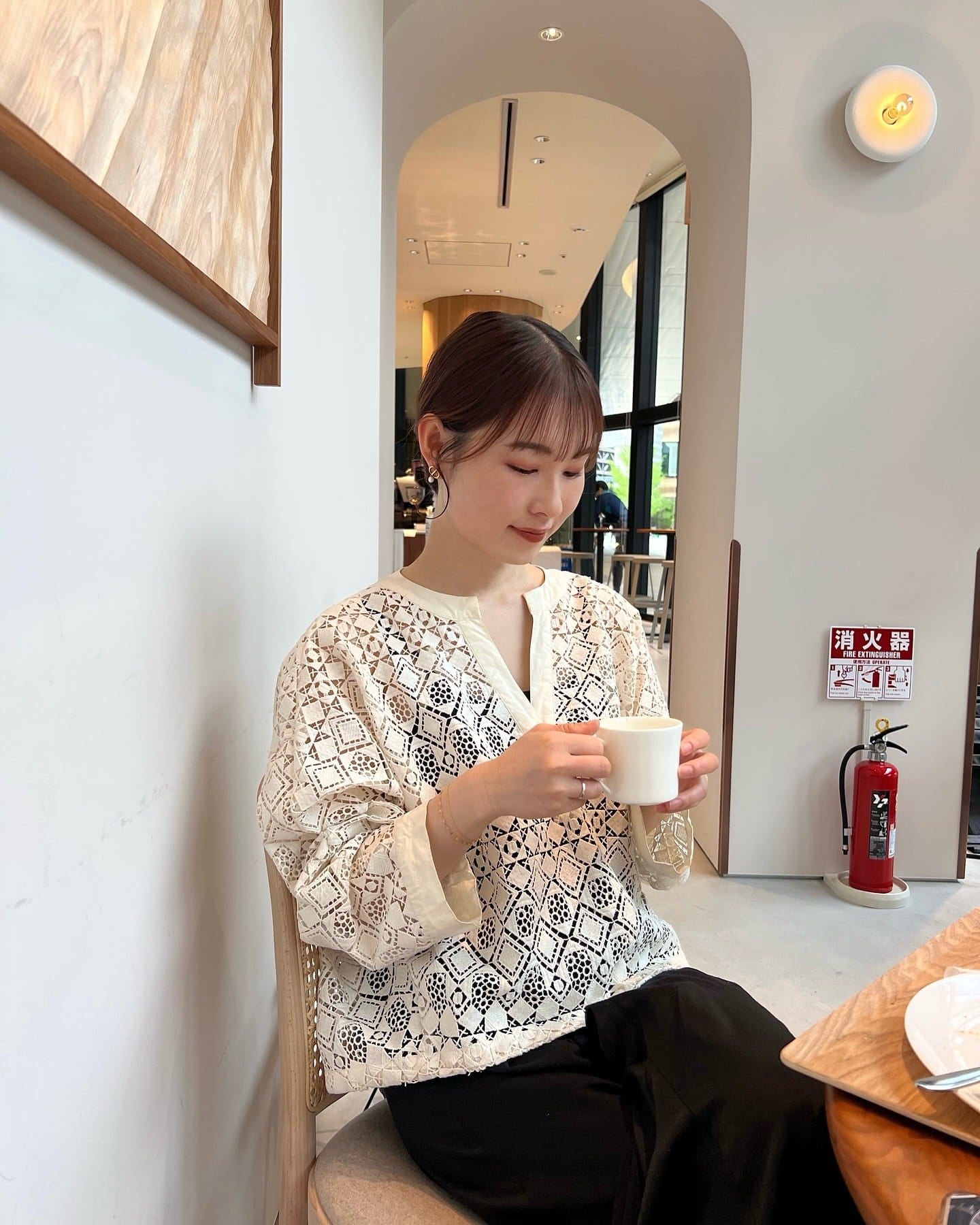 カフェでコーヒーを楽しむ女性のブレスレット着用コーディネート｜レースブラウス×華奢ゴールド