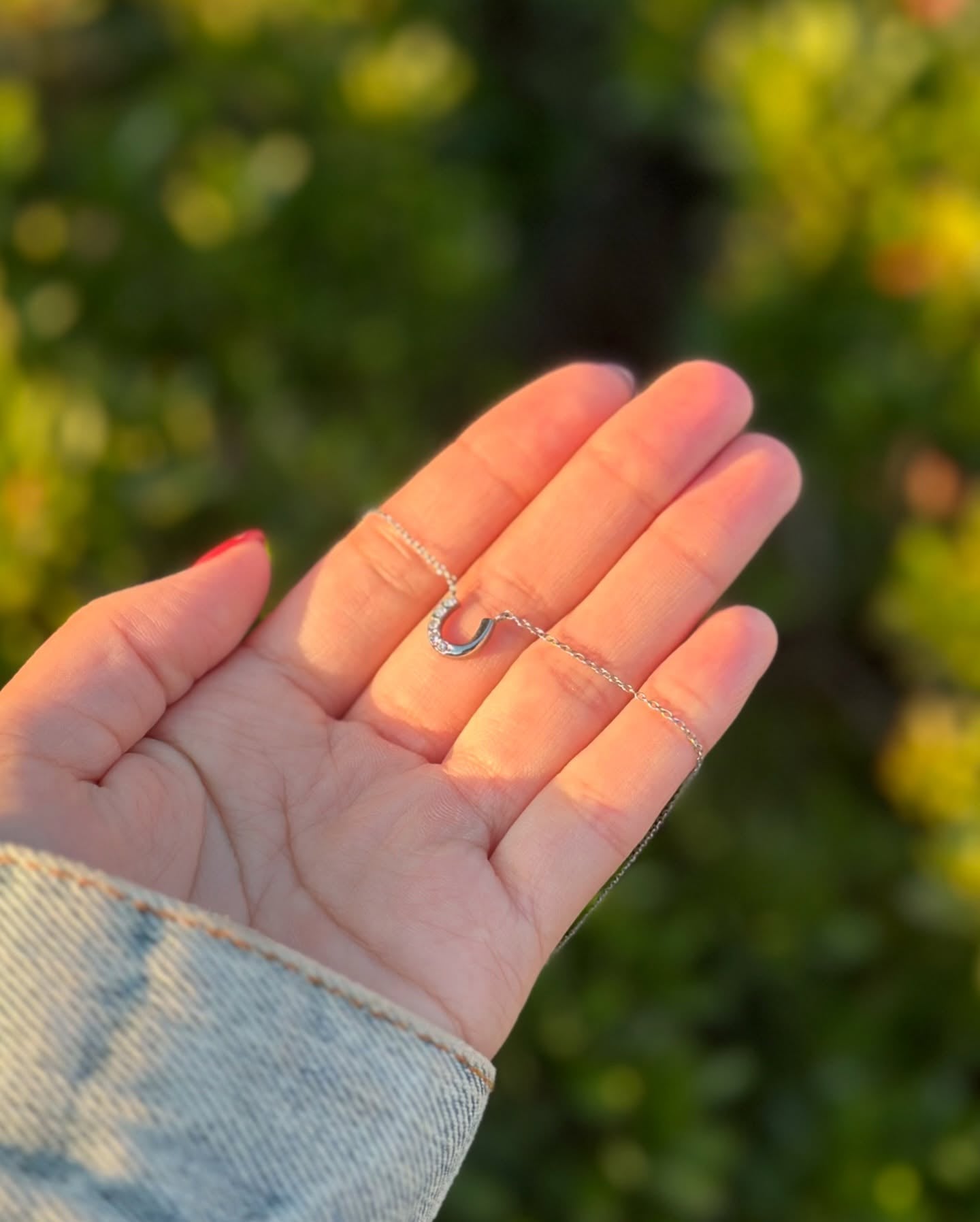 夕日の光に照らされたシルバーのホースシューネックレスのディテール｜手元アップ写真