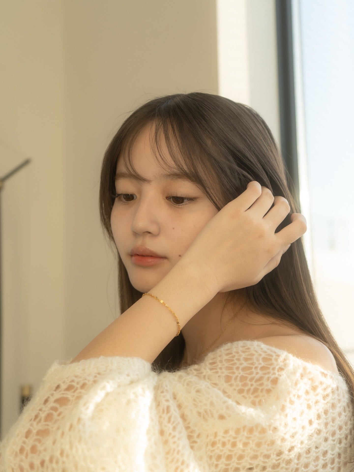 日差しを受けてきらめく、白ニットに合わせた華奢なゴールドブレスレット