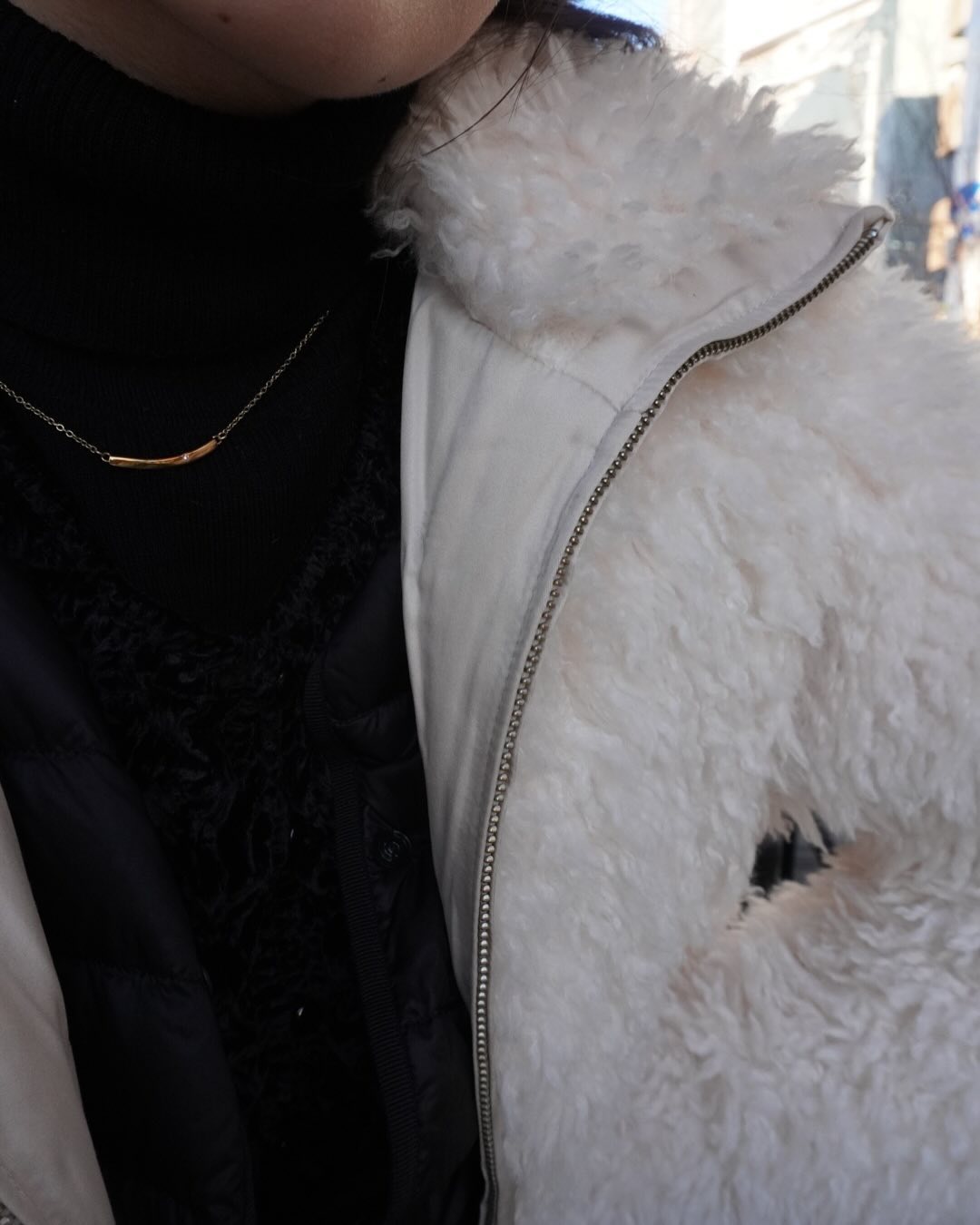 黒タートルネックの上で上品に輝くゴールドのバーネックレスとホワイトボアアウターの寄り