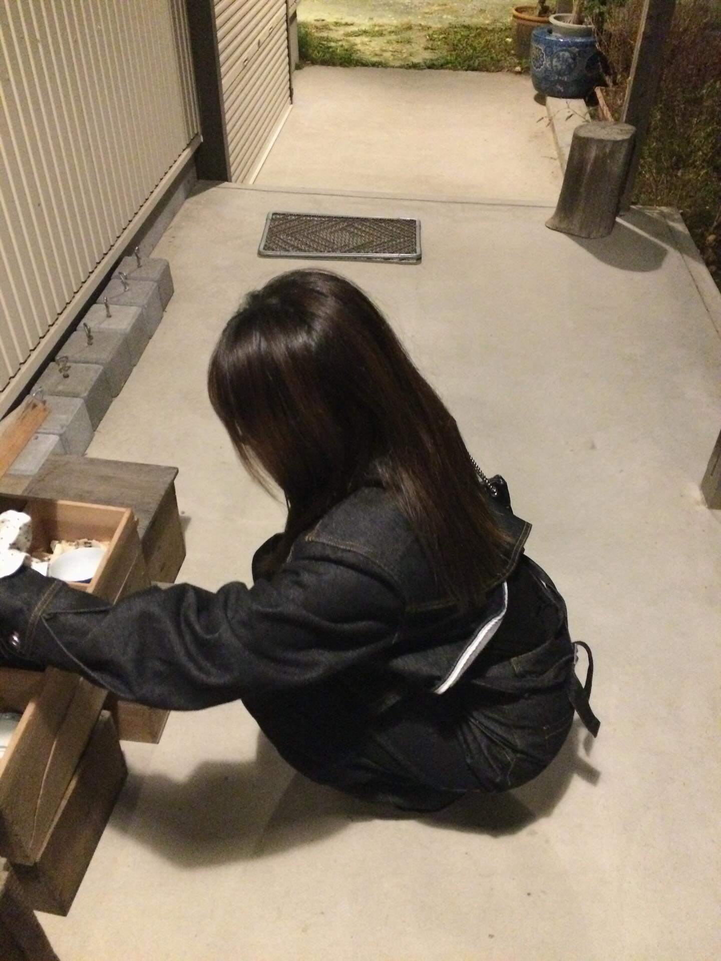 夜の屋外でしゃがむ後ろ姿のデニムコーデ。黒バッグと合わせたラフなムードが印象的。